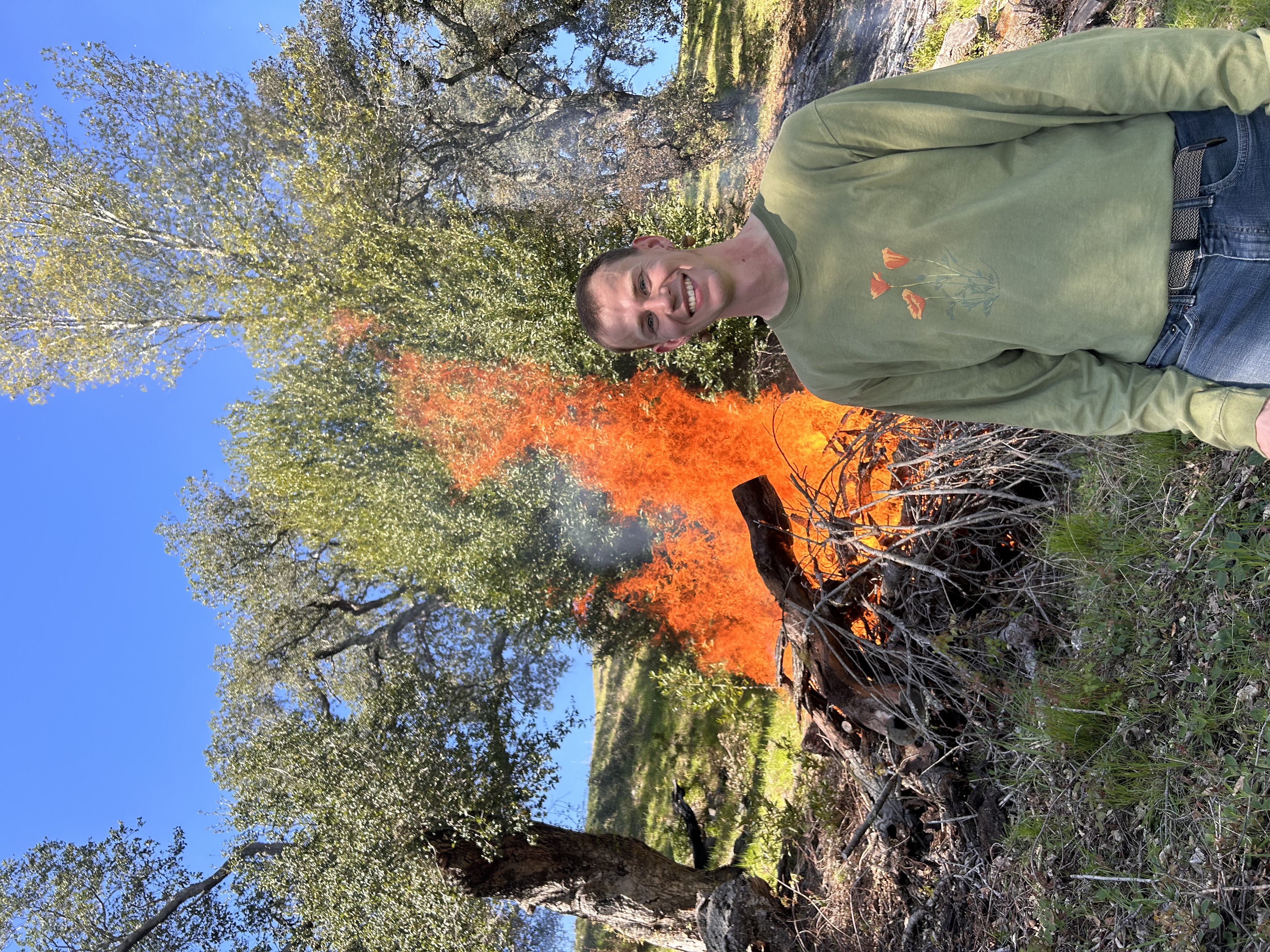 Nick Thayer in front of a burning field with trees around it.